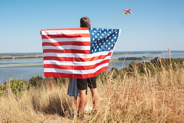 Gelukkige kinderen spelen met Amerikaanse vlag spelen in de natuur en lanceren een vlieger in de lucht