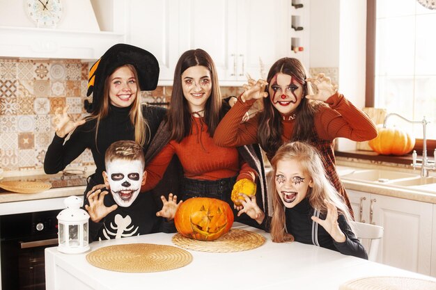 Gelukkige kinderen vieren Halloween in de keuken thuis in kostuums en make-up met pompoen lantaarn jack