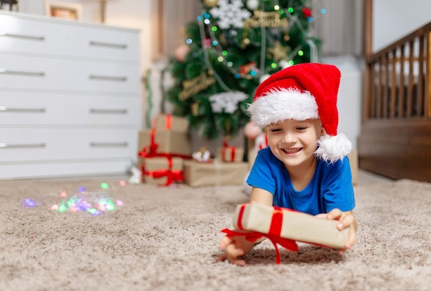 Gelukkige kindjongen ontvangt op kerstochtend een cadeautje dat op een gezellig tapijt in zijn kamer in pyjama ligt