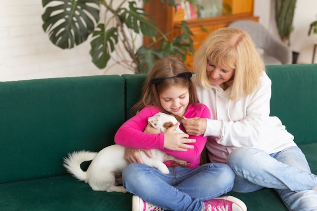 Gelukkige kleindochter en grootmoeder zittend op de bank met jack russell terrier hond oma knuffels