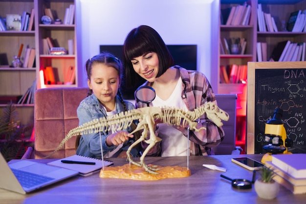 Gelukkige kleine dochter en haar moeder bestuderen fossiele dieren met een vergrootglas