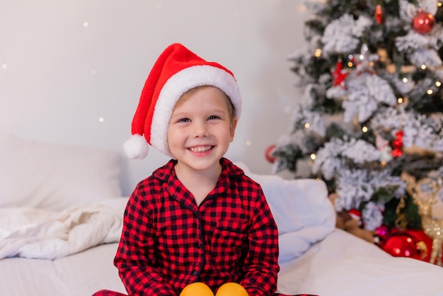 gelukkige kleine jongen in pyjama en kerstmuts thuis in bed mandarijnen eten voor Kerstmis