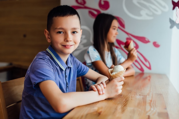 Gelukkige kleine jongen, ontspannen met ijs in handen op café met zijn vriendin.