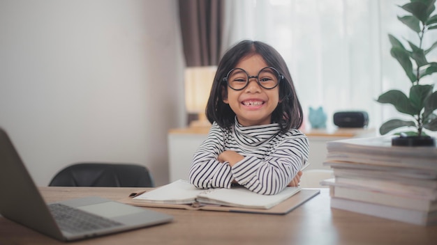 Foto gelukkige kleine meisje studeert online met behulp van een laptop thuis glimlachend klein kind beveelt les of les aan