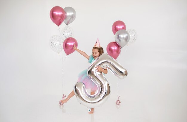 Gelukkige kleine verjaardag meisje dansen met ballonnen en folie nummer vijf op een witte achtergrond