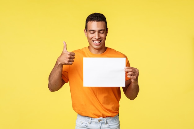 Gelukkige knappe Spaanse kerel in oranje t-shirt, die leeg document houdt