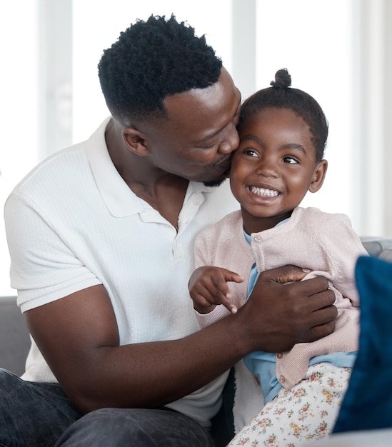 Gelukkige kus en zwarte man met kind op de bank voor binding ontspannen en knuffelen in de woonkamer glimlach liefde en Afrikaanse vader omhelzen meisje kind met zorg rusten in de lounge voor familie tijd thuis