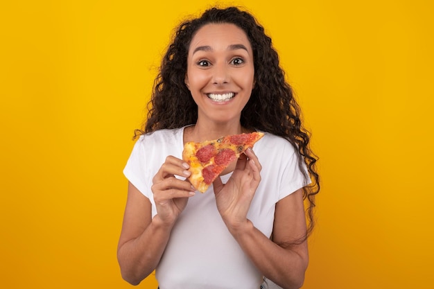 Gelukkige latijnse dame die pizzaplak houdt bij studio