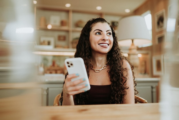 Gelukkige Latijnse dame ontspant alleen thuis pose en deelt goed nieuws op sociale media via mobiele telefoon.