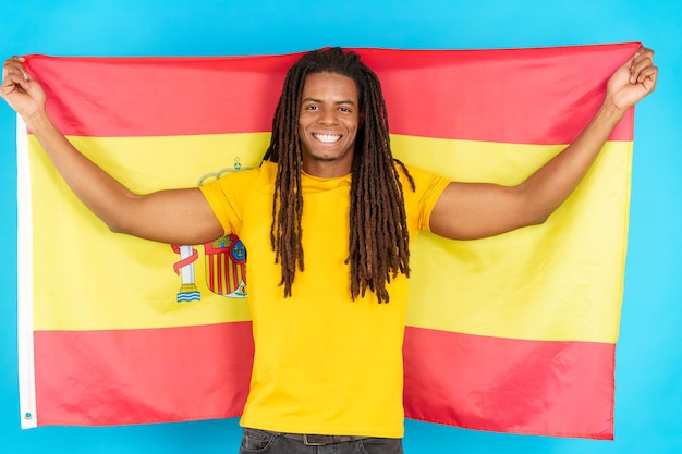 Gelukkige Latijnse mens die met dreadlocks een Spaanse nationale vlag opheffen