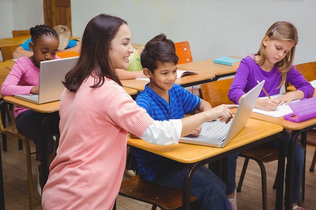 Gelukkige leraar die laptop met student met behulp van