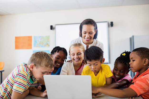 Gelukkige leraar en leerlingen die laptop met behulp van