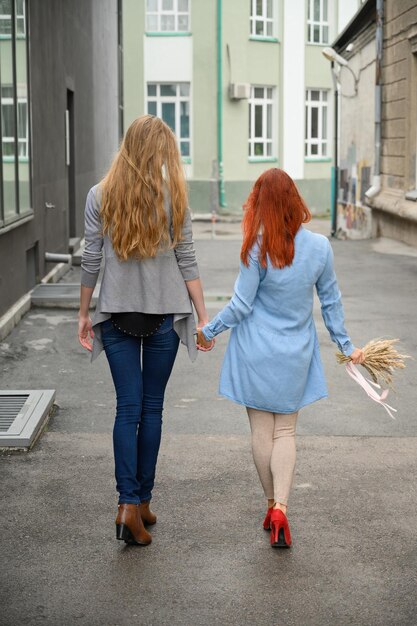 Gelukkige lesbische koppel die hand in hand door de straat lopen de rug van twee mooie vrouwen op een date met een boeket gedroogde bloemen LGBT