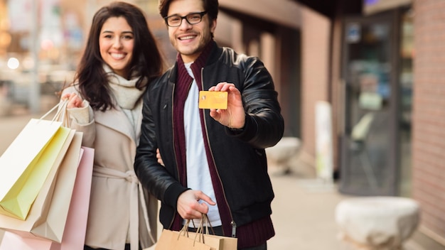 Gelukkige man die creditcard toont na het winkelen met zijn vrouw