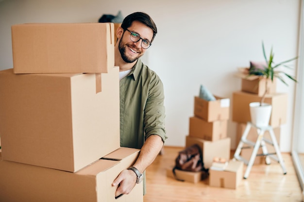 Gelukkige man die stapel kartonnen dozen draagt terwijl hij verhuist naar een nieuw appartement