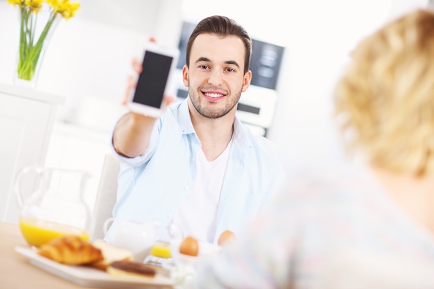 gelukkige man die zijn smartphone laat zien tijdens het ontbijt