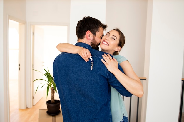 Gelukkige man die zijn vrouw knuffelt terwijl ze de sleutels van hun nieuwe huis vasthoudt.