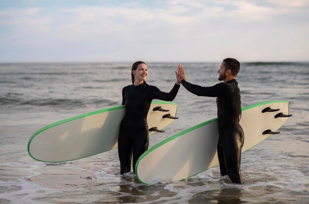 Gelukkige man en vrouw in wetsuits geven elkaar een high-five na het samen surfen.
