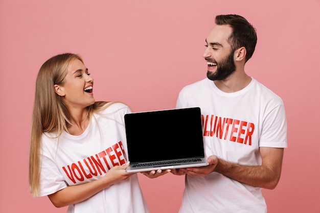 gelukkige man en vrouw vrijwilligers die uniforme t-shirts dragen met een geïsoleerd laptopscherm