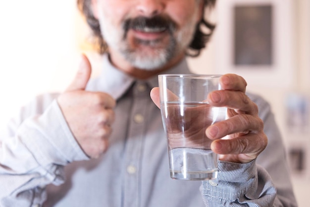 Gelukkige man geeft aanbevelingen voor een gezonde levensstijl en geniet thuis van kristalhelder water