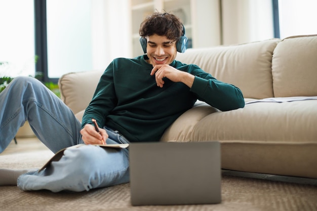 Foto gelukkige man in de buurt van laptop die aantekeningen maakt die thuis online leert