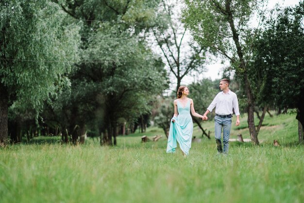 Gelukkige man in een wit overhemd en een vrouw in een turquoise jurk wandelen in het bospark