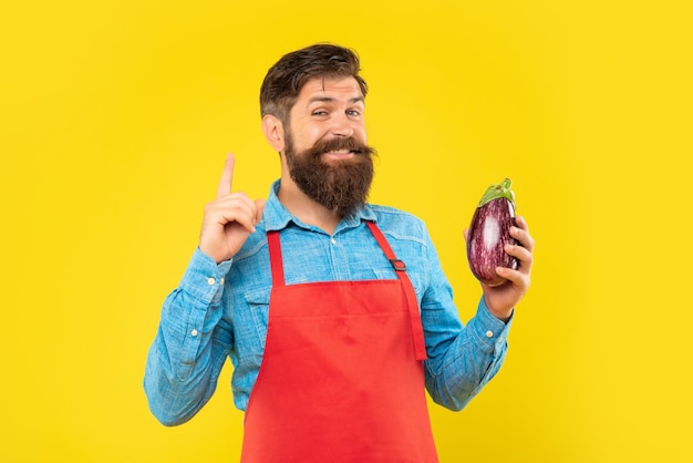 Gelukkige man met aubergine in schort kreeg idee om vinger op gele achtergrond te houden winkelier