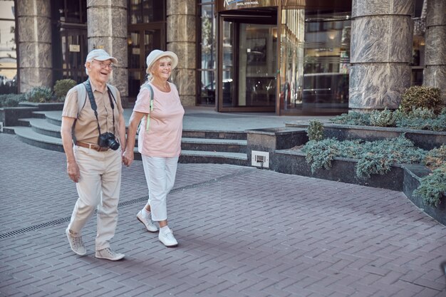 Gelukkige man met een digitale camera en een stijlvolle oudere dame die hand in hand loopt