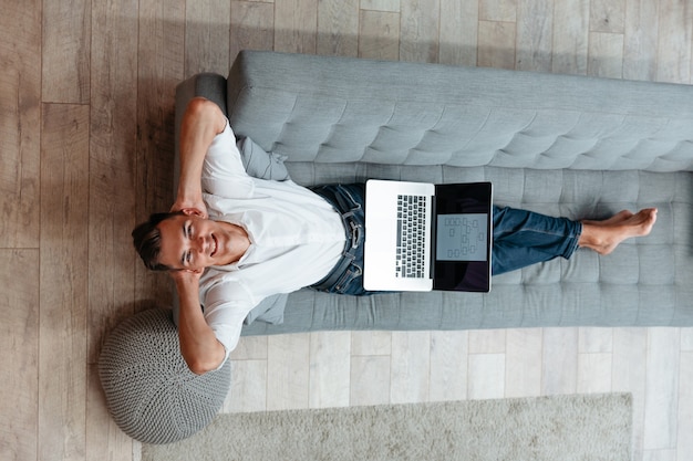 Gelukkige man met een laptop die op de bank rust