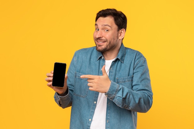 Gelukkige man met een smartphone die op een scherm op een gele achtergrond wijst