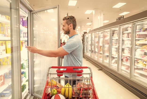 Gelukkige man met winkelwagentje klant consument met aankopen man bij supermarkt shopper bij boodschappen eten kopen bij supermarkt consumptie