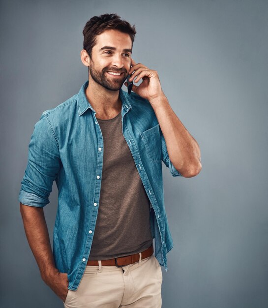 Gelukkige man mode en stijl in telefoongesprek met trendy vrolijk in studio op grijze achtergrond Mannelijke persoon glimlach en outfit voor vertrouwen detailhandel of verkoop in communicatie voor promo in denim shirt