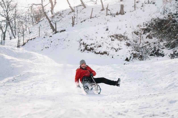 Gelukkige man op een slee op een met sneeuw bedekte heuvel in de winter
