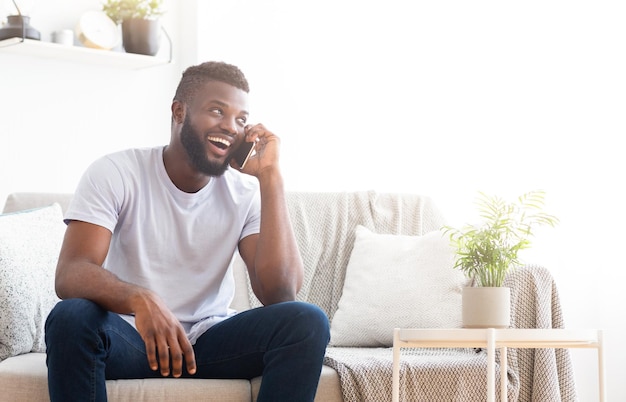 Gelukkige man praat aan de telefoon terwijl hij op de bank zit