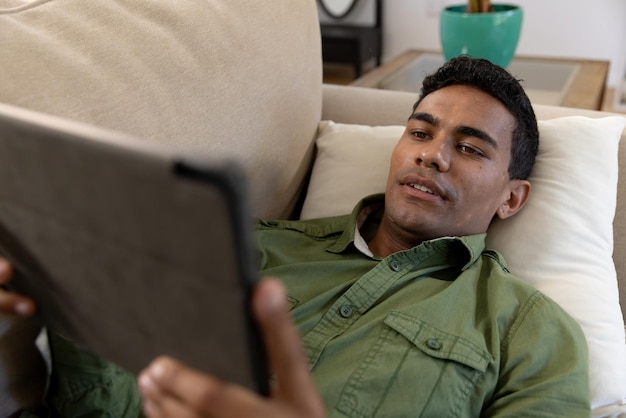 Gelukkige man van twee rassen die op de bank ligt en thuis een tablet gebruikt