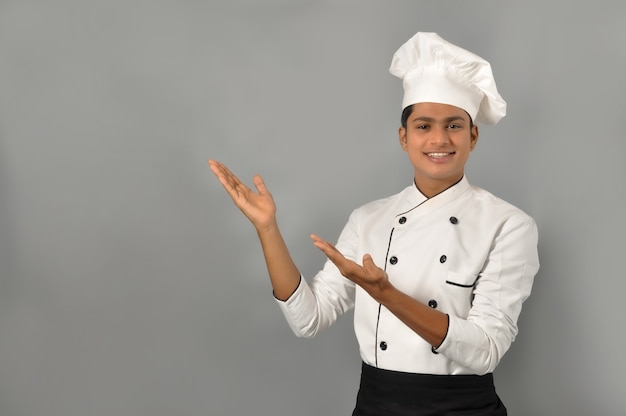 Gelukkige mannelijke Indische chef-kok die met zijn handen op een grijze muur richt