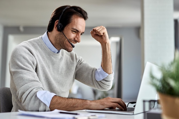 Gelukkige mannelijke ondernemer die een e-mail op laptop leest en goed nieuws viert