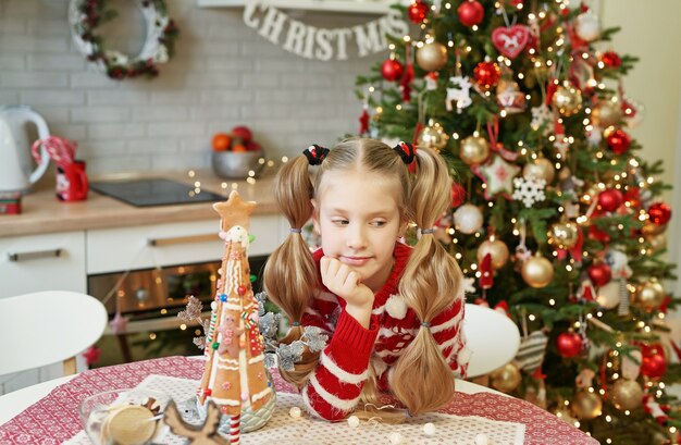 Gelukkige meisjezitting bij lijst in binnenlandse keuken met kerstboom