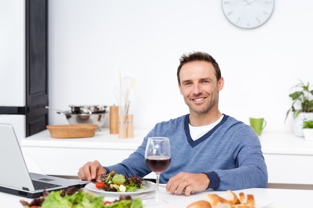 Gelukkige mens die aan zijn laptop werkt terwijl het hebben van lunch