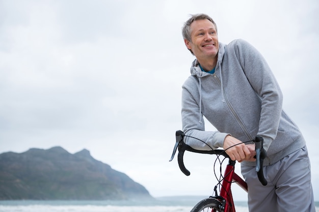 Gelukkige mens die op fiets bij strand leunt