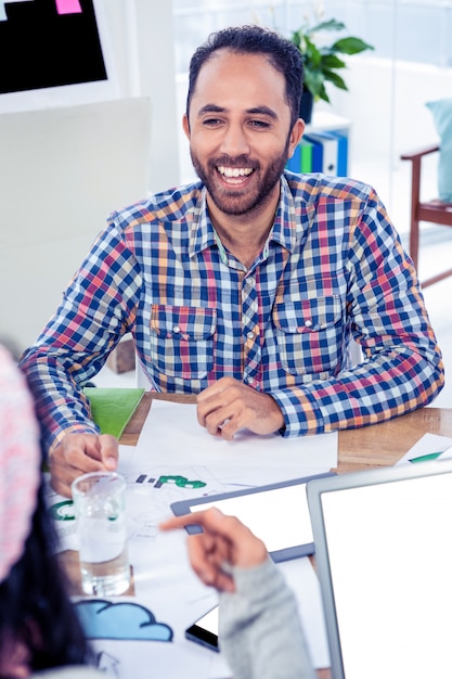 Gelukkige mens die terwijl het bekijken collega in creatief bureau glimlacht