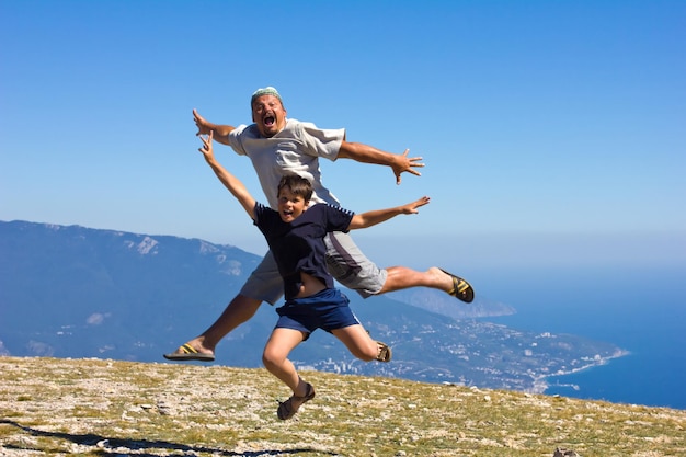 Gelukkige mens en jongen die op een achtergrond van bergen en hemel springen