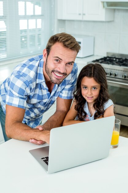 Gelukkige mens met dochter die laptop in keuken met behulp van