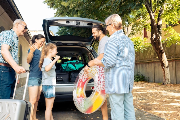 Gelukkige mensen die met het voertuig aan zee reizen, vertrekken op vakantiereis met ouders, grootouders en klein meisje. Bagage en koffer laden in auto kofferbak, zomeravontuur.