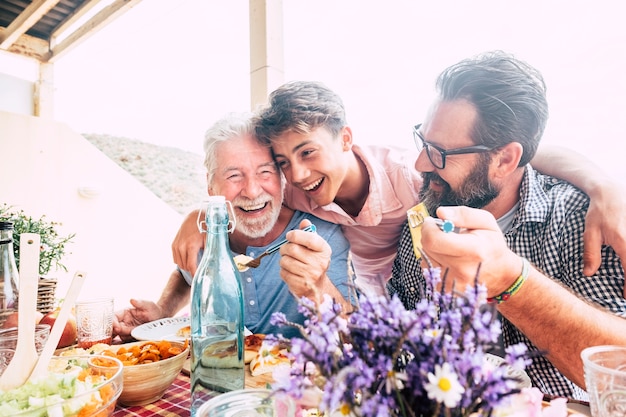 Gelukkige mensen familie concept lachen en plezier hebben samen met drie verschillende generaties leeftijden: grootvader vader en jonge tienerzoon allemaal samen eten tijdens de lunch