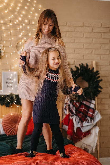 Gelukkige moeder en dochter dansen op bed, in afwachting van Kerstmis, vreugdevolle feestdagen, mooie decoratie op de achtergrond