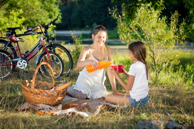 Gelukkige moeder en dochter die jus d'orange drinken bij picknick