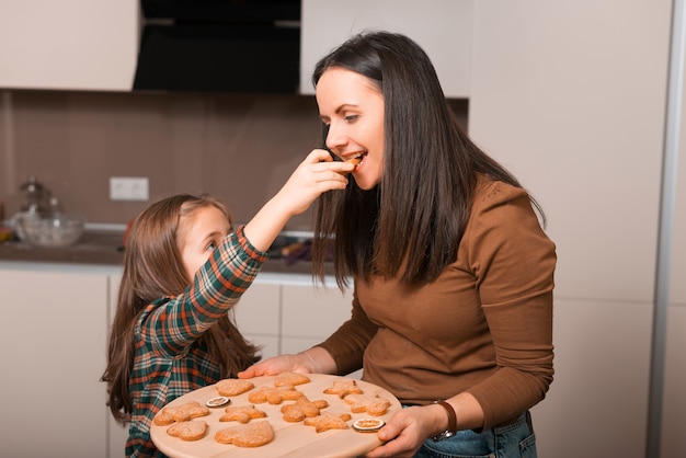 Gelukkige moeder en dochter die net gebakken koekjes in keuken proeven