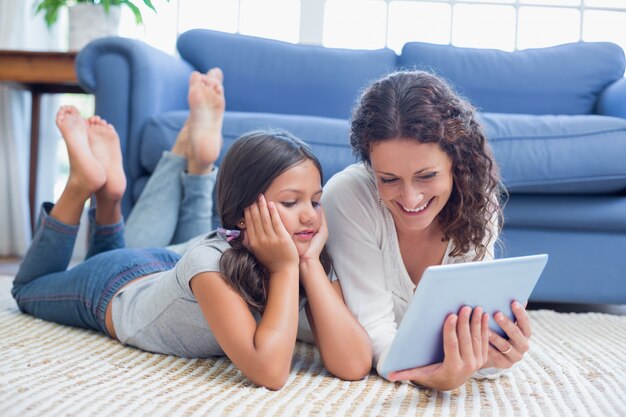 Gelukkige moeder en dochter die op de vloer liggen en tablet gebruiken