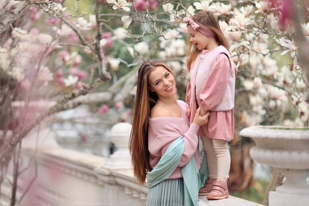 Gelukkige moeder en dochter op een wandeling in het park in roze kleren met plezier onder de bloeiende magnoliabomen.